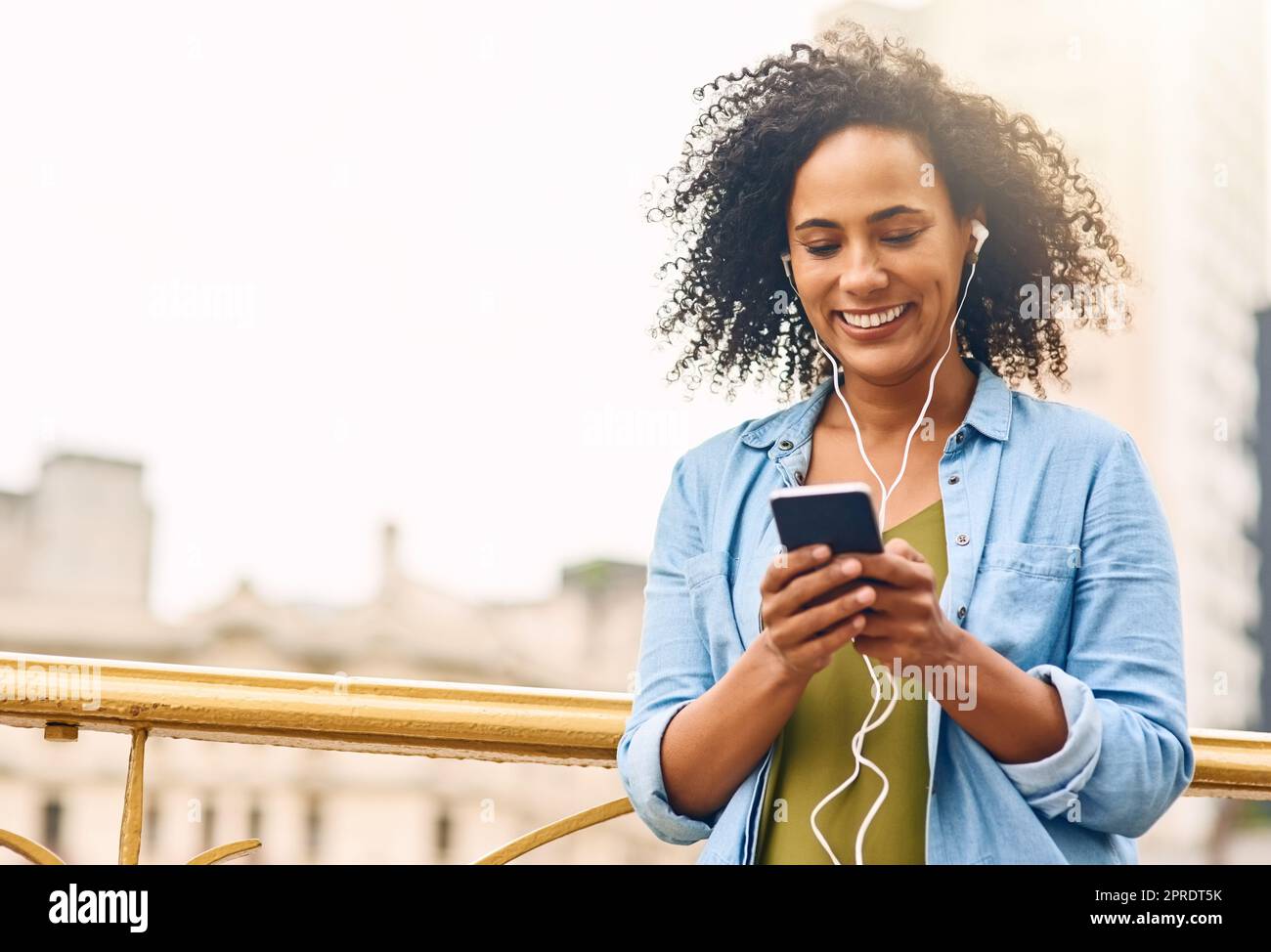 Une jeune femme qui écoute de la musique sur son téléphone portable lorsqu'elle est en ville s'est amusée en déplacement. Banque D'Images