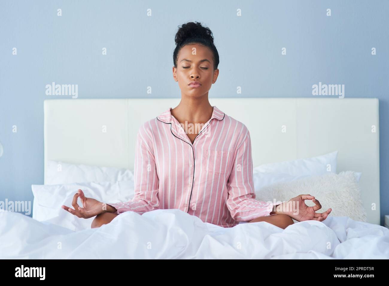 Prenez toujours le temps de méditer. Une jeune femme attirante méditant au lit à la maison. Banque D'Images