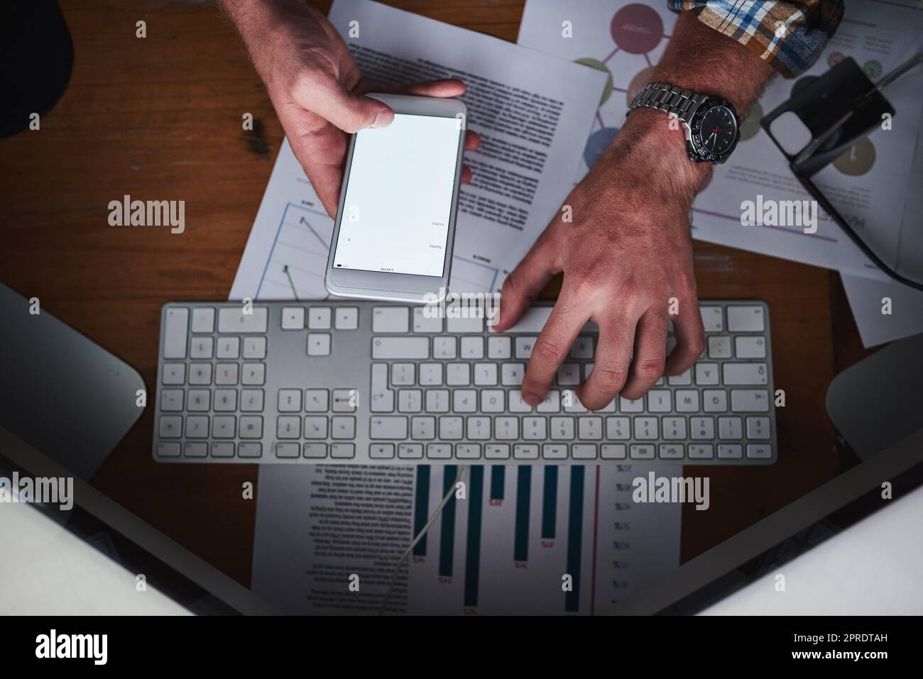 Les mains sur un clavier d'ordinateur et la saisie sur un téléphone dans un bureau avec travail de papier par dessus. Gros plan d'un homme d'affaires qui navigue sur Internet, termine un rapport ou envoie un e-mail de communication Banque D'Images