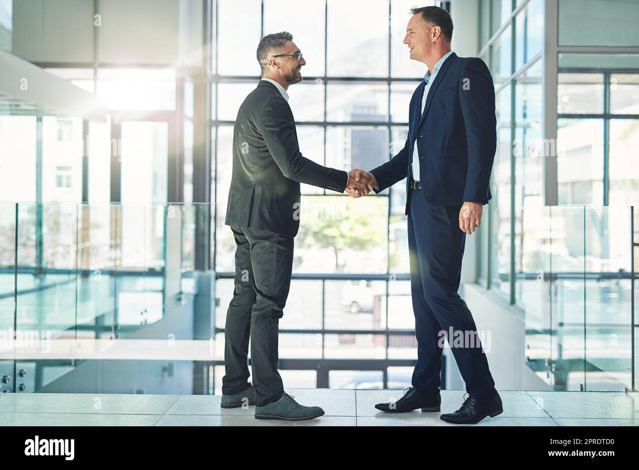 Les hommes d'affaires d'entreprise souriants et confiants échangent des poignée de main dans la fusion de confiance mondiale, qui se réunit au sein d'une entreprise moderne. Les cadres professionnels de la conférence sur les accords de développement commercial de l'entreprise Banque D'Images