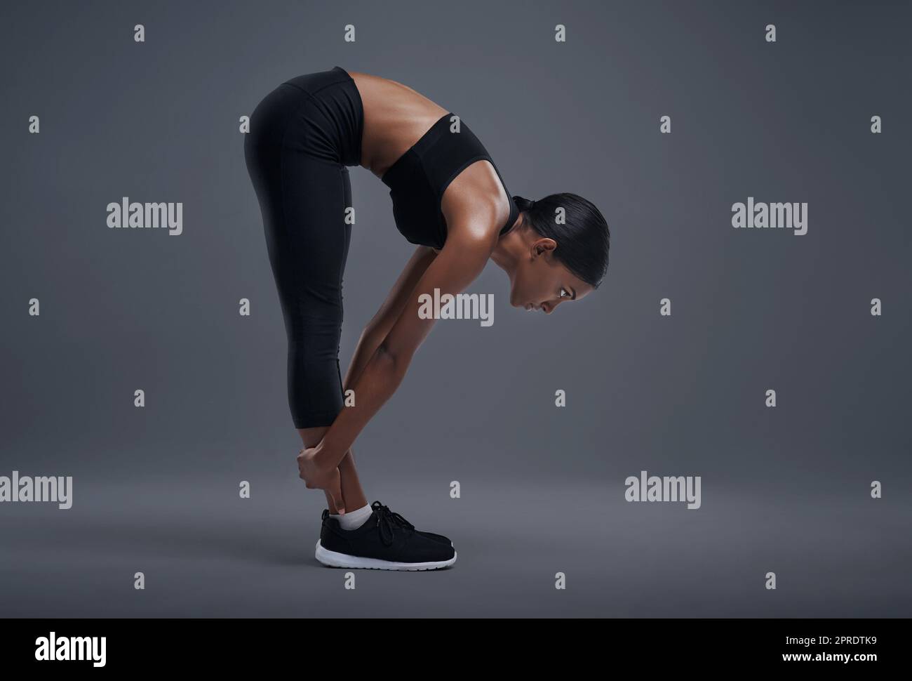 Elle augmente sa flexibilité grâce à sa forme physique. Photo en studio d'une jeune femme sportive s'exerçant sur un fond gris. Banque D'Images