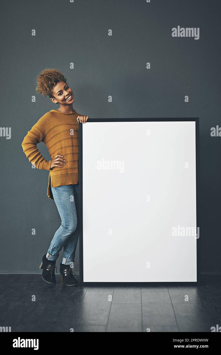 Jeune femme tenant et montrant un signe vide ou vierge pour faire une idée ou une annonce publicitaire. Styliste heureux, excités et gai debout avec maquette de tableau blanc ou de bannière d'espace de rédaction. Banque D'Images