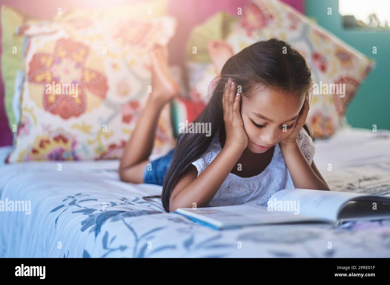 Perdu dans le monde magique des mots. Une adorable petite fille lisant un livre à la maison. Banque D'Images