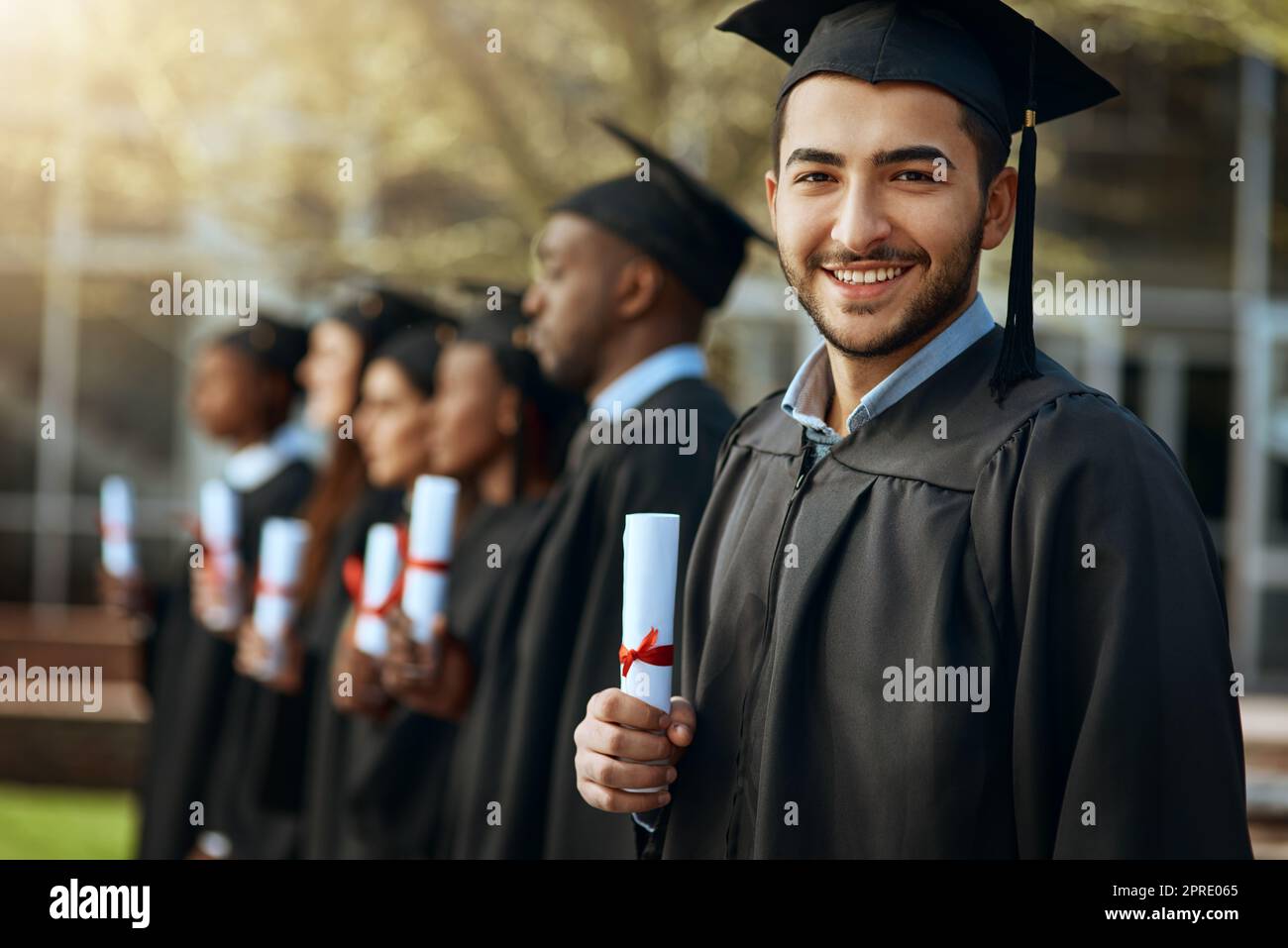 Notre plus grand accomplissement à ce jour. Portrait d'un jeune homme titulaire de son diplôme en se tenant debout avec ses camarades le jour de la remise des diplômes. Banque D'Images