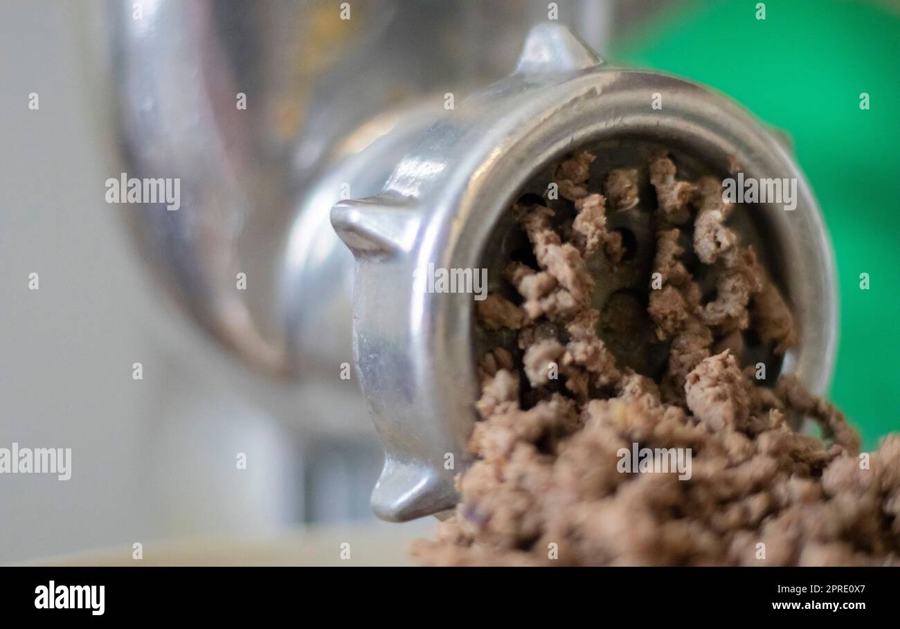 Hachez la viande hachée dans un moulin à viande mécanique manuel. La viande fraîche bouillie est hachée avec un vieux moulin à viande en métal, en gros plan dans la cuisine. Banque D'Images