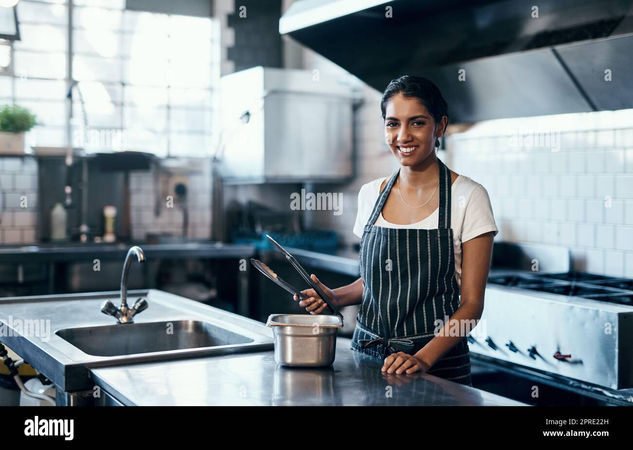 Cuisiner, faire de la nourriture et travailler comme chef dans une cuisine commerciale avec des pinces et de l'équipement industriel. Portrait d'une femme cuisinier préparant un repas pour le déjeuner, le dîner ou le souper dans un restaurant ou un café Banque D'Images