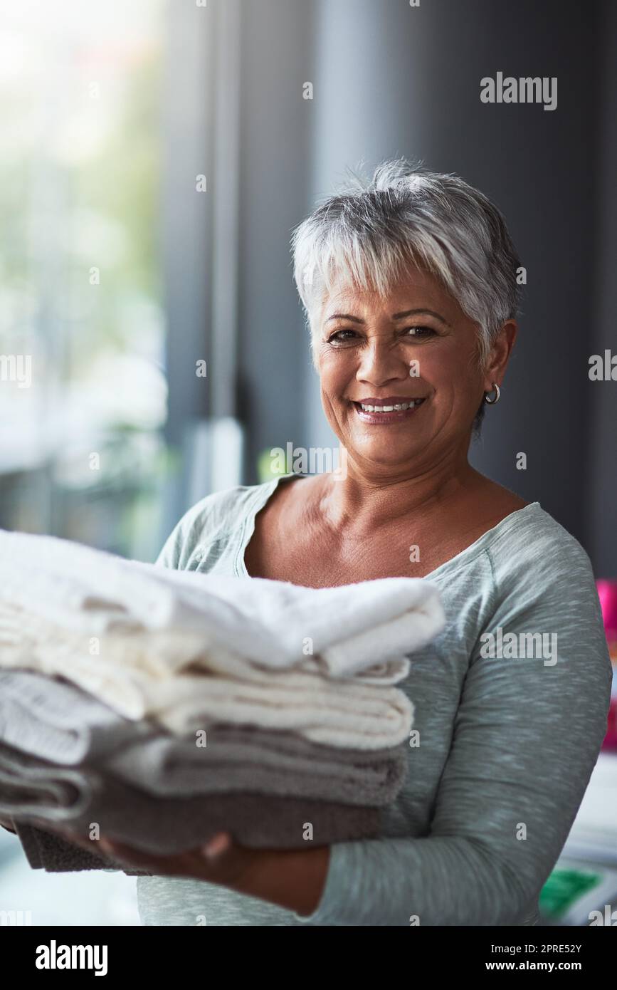 Tout le monde appelle pour des serviettes fraîchement lavées. Portrait d'une femme mûre tenant des serviettes fraîchement pliées tout en faisant la lessive à la maison. Banque D'Images