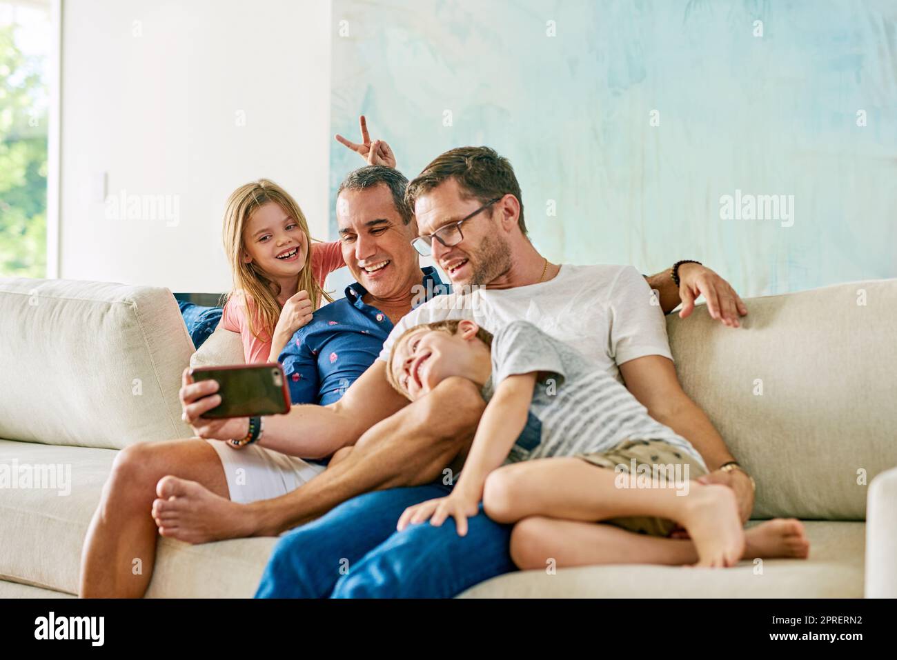 Prendre des selfies stupides sur le canapé. Une famille affectueuse de quatre personnes prenant des selfies sur le canapé à la maison. Banque D'Images