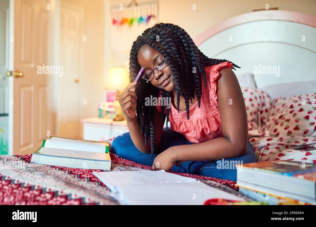 Elle prend son travail scolaire au sérieux. Une adorable petite fille qui fait ses devoirs sur son lit dans sa chambre. Banque D'Images
