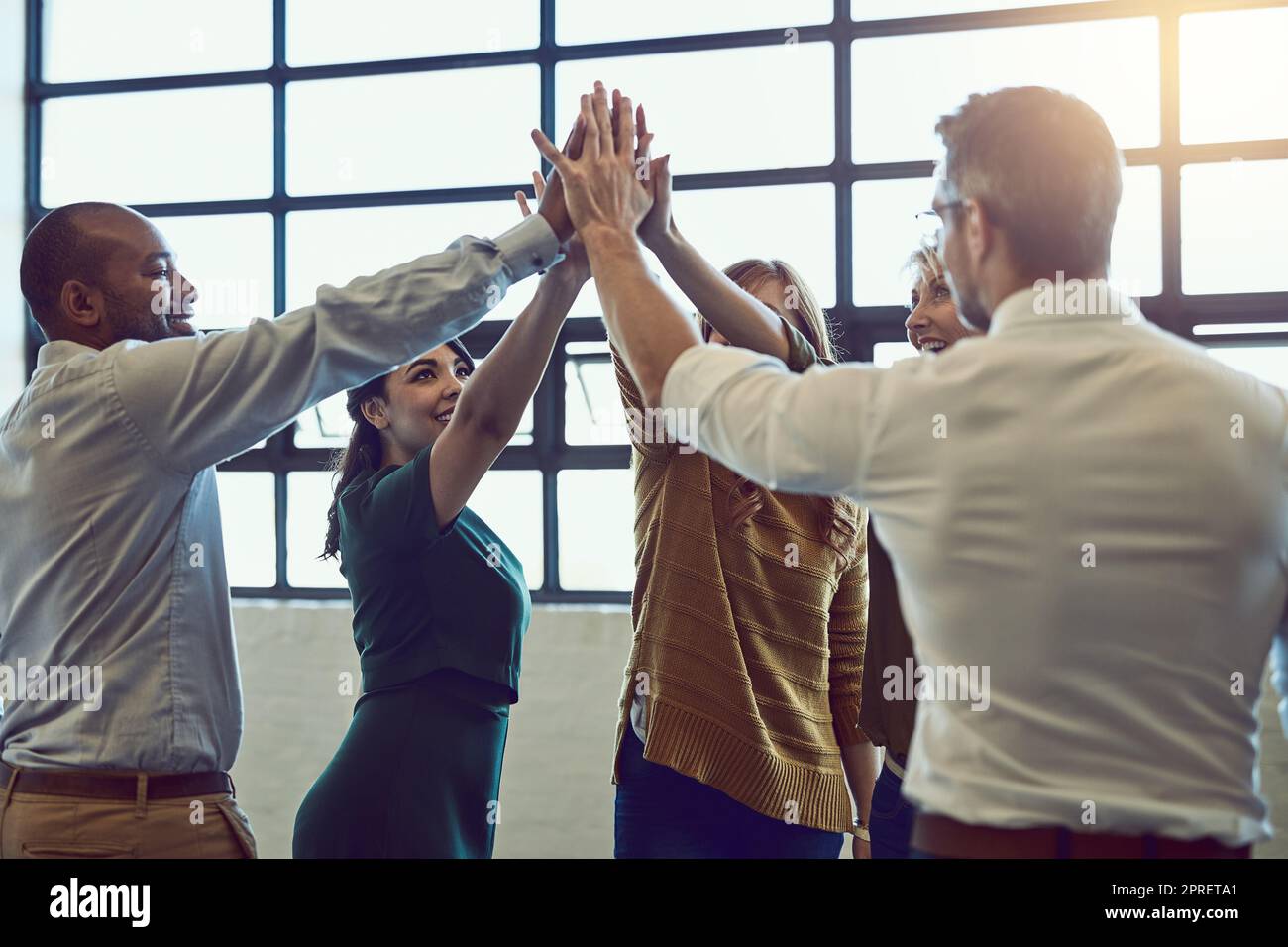 Une équipe de collègues joyeux fête avec cinq hauts après avoir entendu de bonnes nouvelles au bureau. Équipe diversifiée gagnant et soutenant les uns les autres. Des gens professionnels et efficaces qui se tiennent ensemble. Banque D'Images