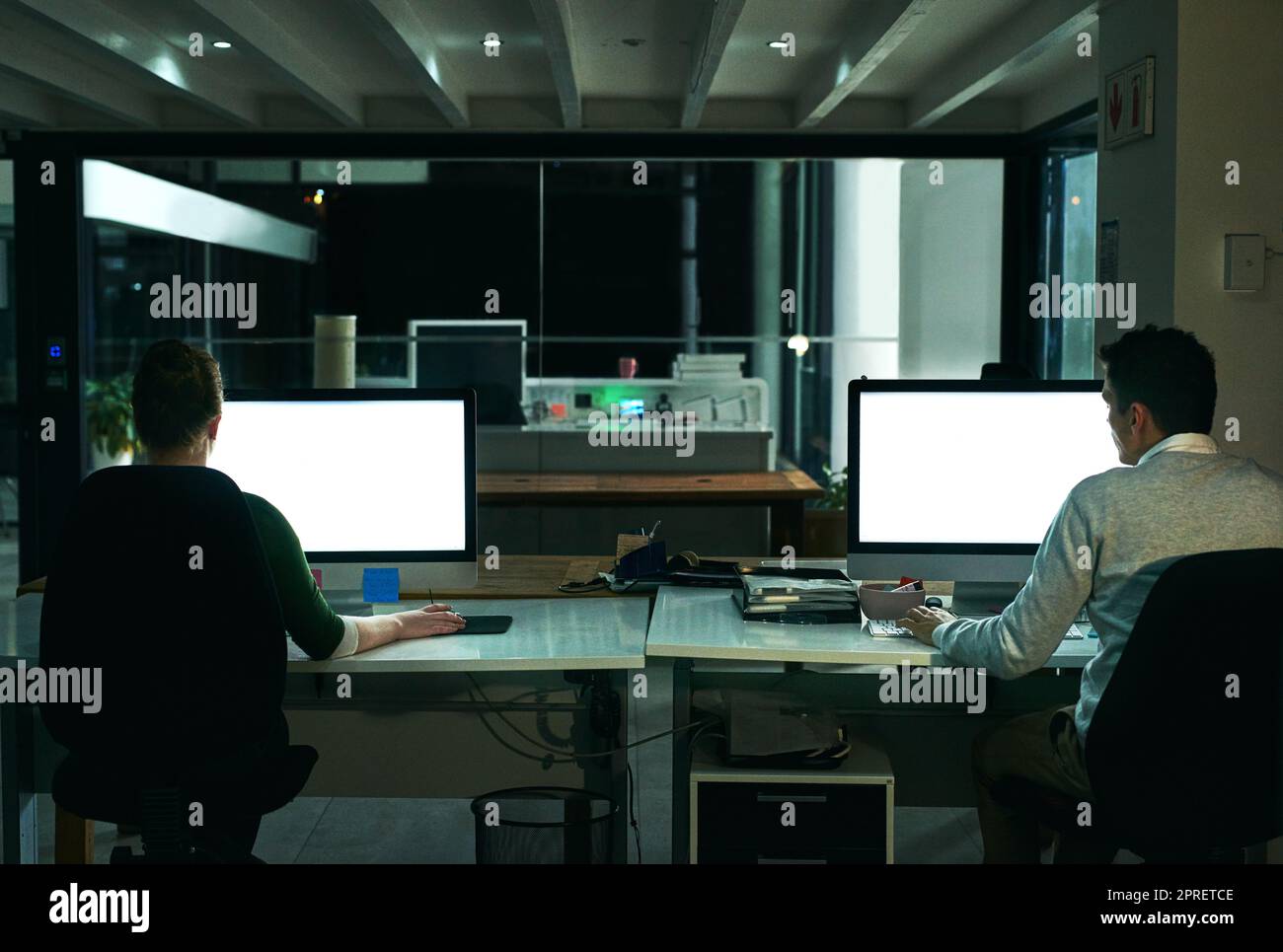 Il est peut-être sombre, mais leur ambition reste brillante. Vue arrière de deux hommes d'affaires travaillant sur des ordinateurs dans un bureau la nuit. Banque D'Images