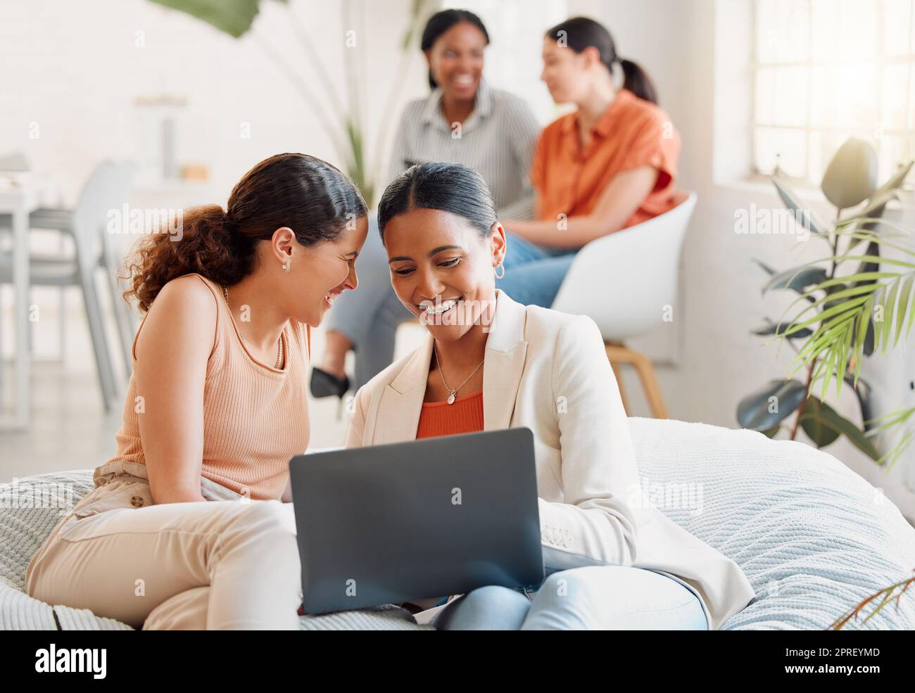 Groupe de femmes d'affaires assis sur un ordinateur portable, en riant en regardant les médias sociaux pendant une pause. Des femmes heureuses se sont encoleuses sur un canapé au travail. Une équipe excitée de filles célébrant un nouvel objectif atteint au démarrage Banque D'Images