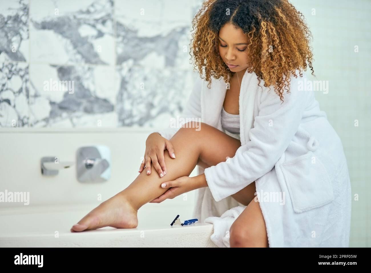 Des jambes douces comme de la soie. Une jeune femme sûre d'elle tient sa jambe fraîchement rasée tout en étant assise dans la salle de bains à la maison. Banque D'Images