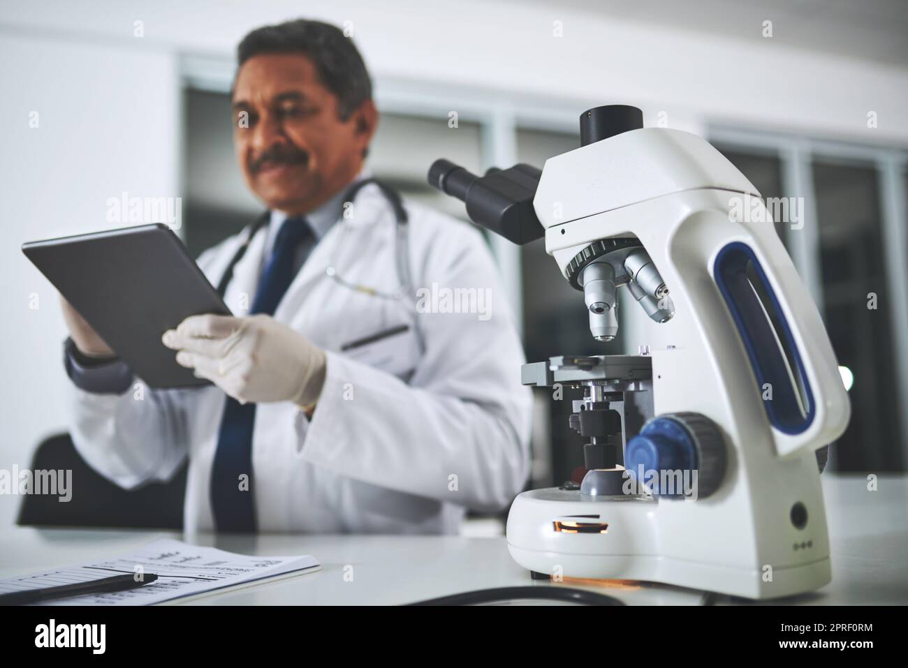 Faire des progrès scientifiques dans le laboratoire. Un microscope sur une table de laboratoire avec un scientifique utilisant une tablette numérique en arrière-plan. Banque D'Images