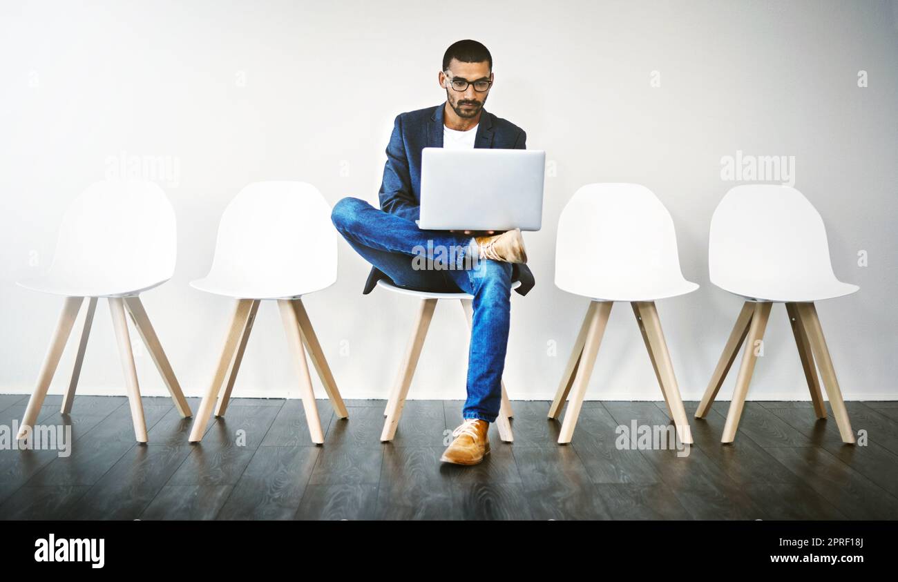 Utiliser Internet pour faire des recherches sur l'entreprise. Un jeune homme d'affaires utilisant un ordinateur portable en attendant dans la file d'attente. Banque D'Images