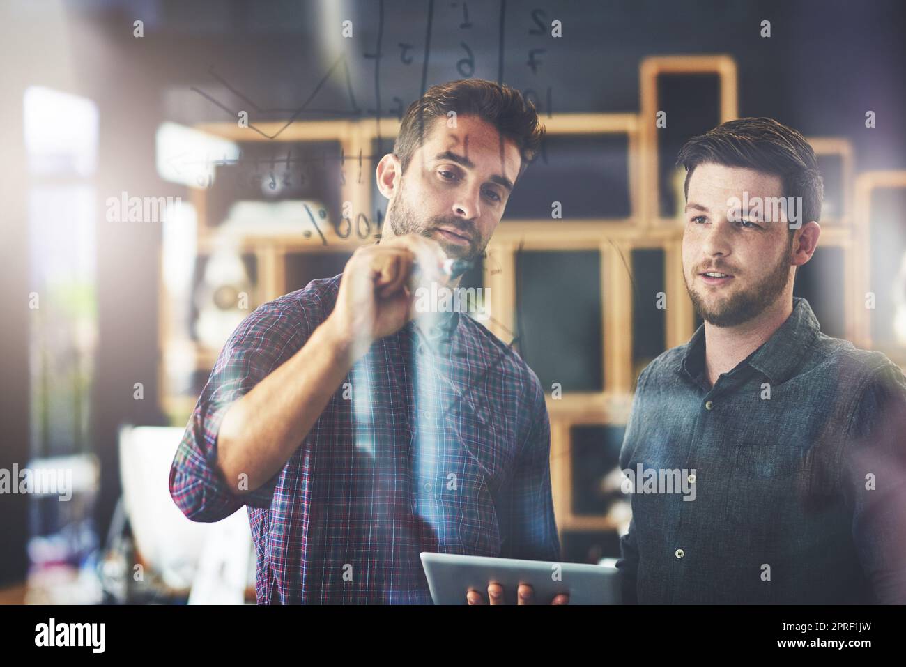 Deux jeunes hommes d'affaires utilisant une tablette numérique et brainstorming sur un mur de verre dans un bureau. Banque D'Images