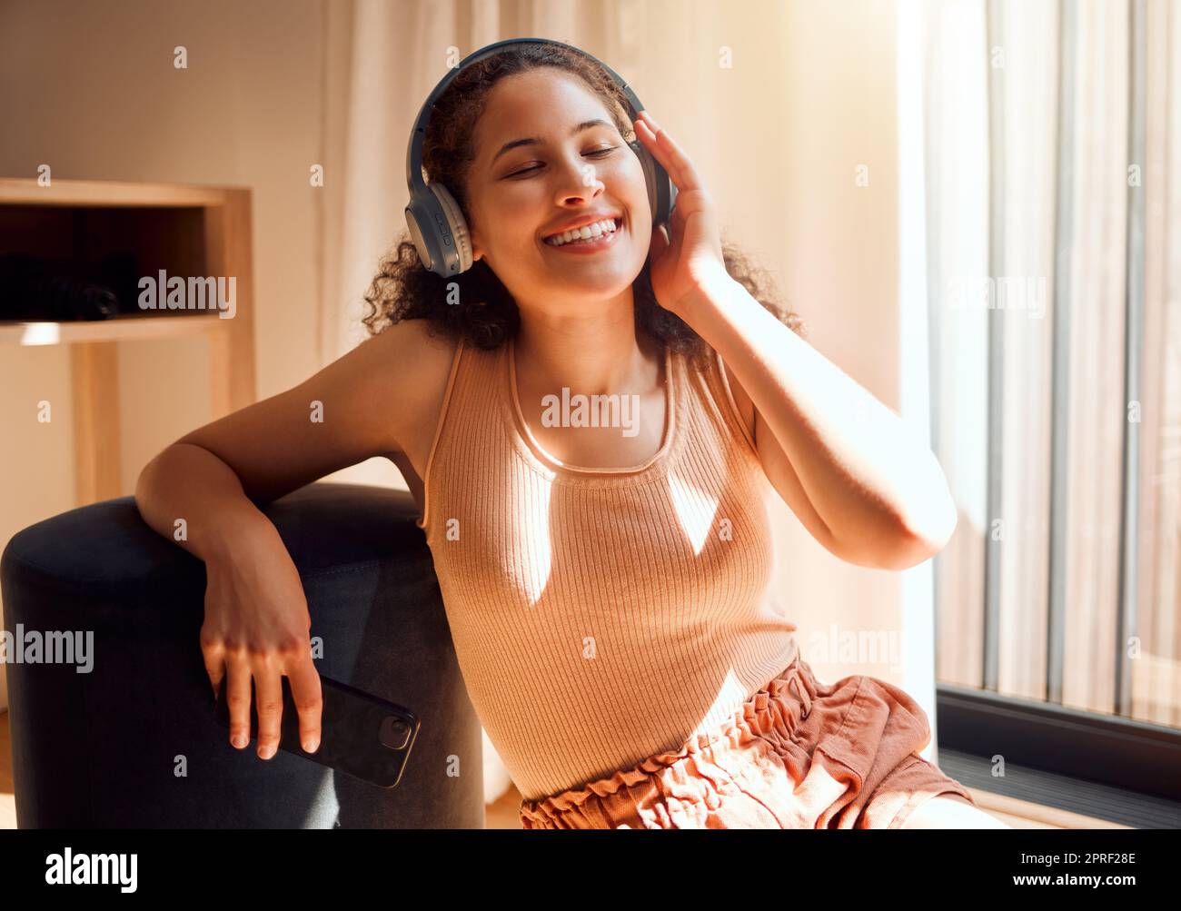 Femme portant un casque pour écouter de la musique, écouter une liste de lecture ou écouter de la musique tout en se détendant à la maison. Jeune fille sympa qui apprécie des chansons sur son port de tête élégant tout en étant assise sur un canapé un week-end Banque D'Images