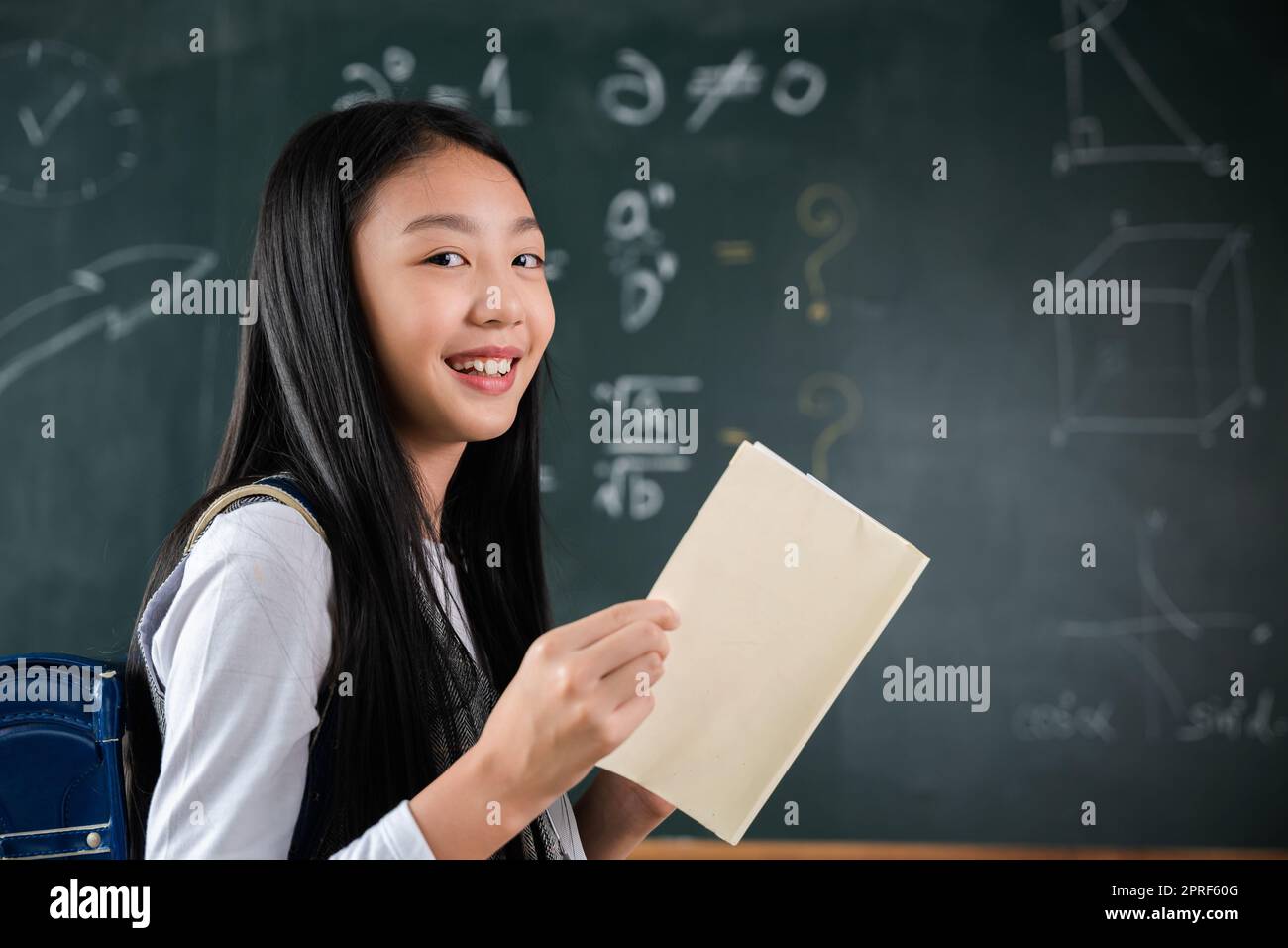 Heureuse belle fille d'école asiatique debout tenant des livres debout devant le tableau noir de la salle de classe Banque D'Images