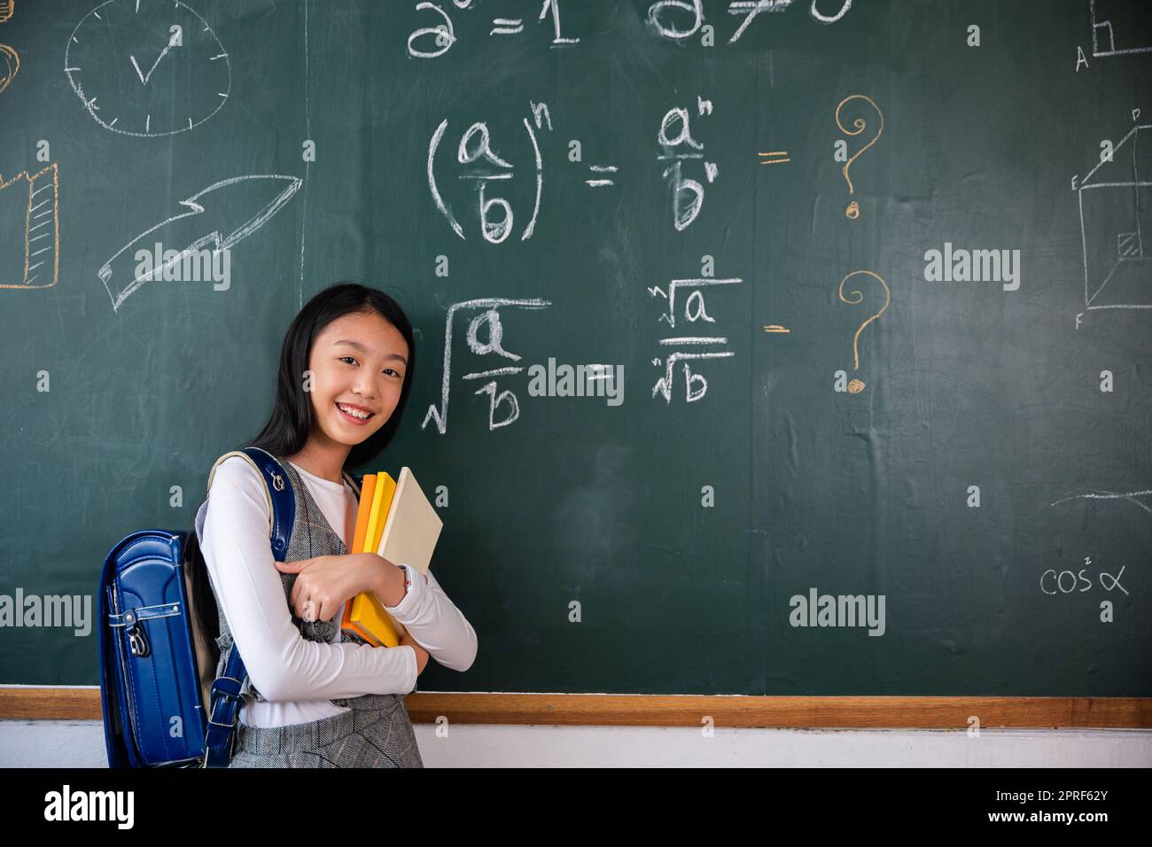 Heureuse belle fille d'école asiatique debout tenant des livres debout devant le tableau noir de la salle de classe Banque D'Images