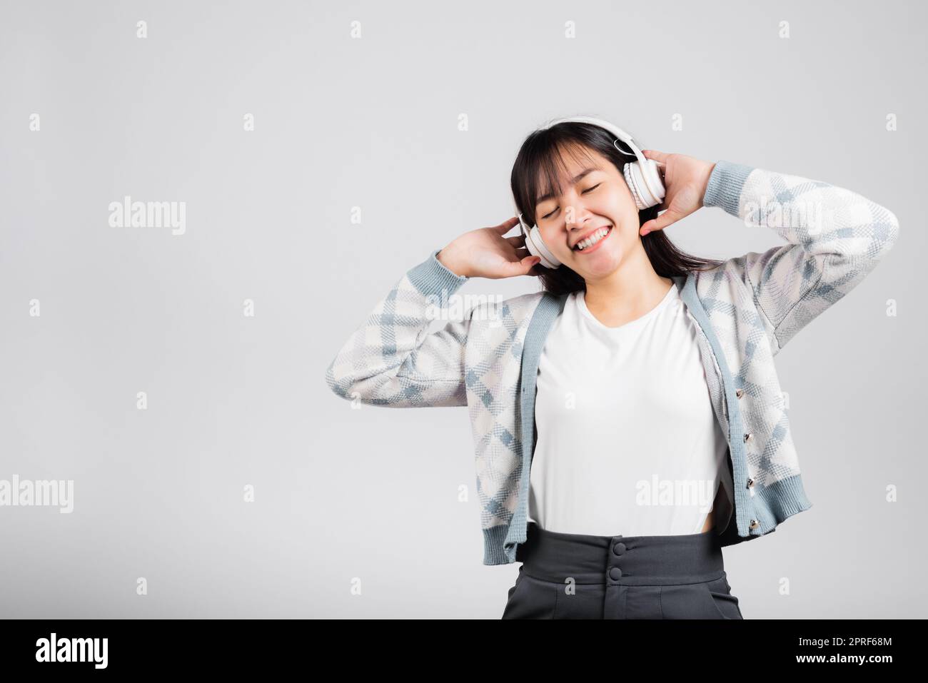 Une femme se réjouit de sourire en écoutant de la radio musicale dans un casque bluetooth et en tenant le téléphone Banque D'Images