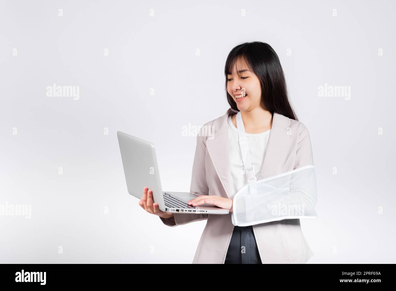 Femme d'affaires asiatique confiante souriante bras cassé après accident et porter une attelle de bras pour le traitement mais elle doit encore travailler elle tient un ordinateur portable Banque D'Images