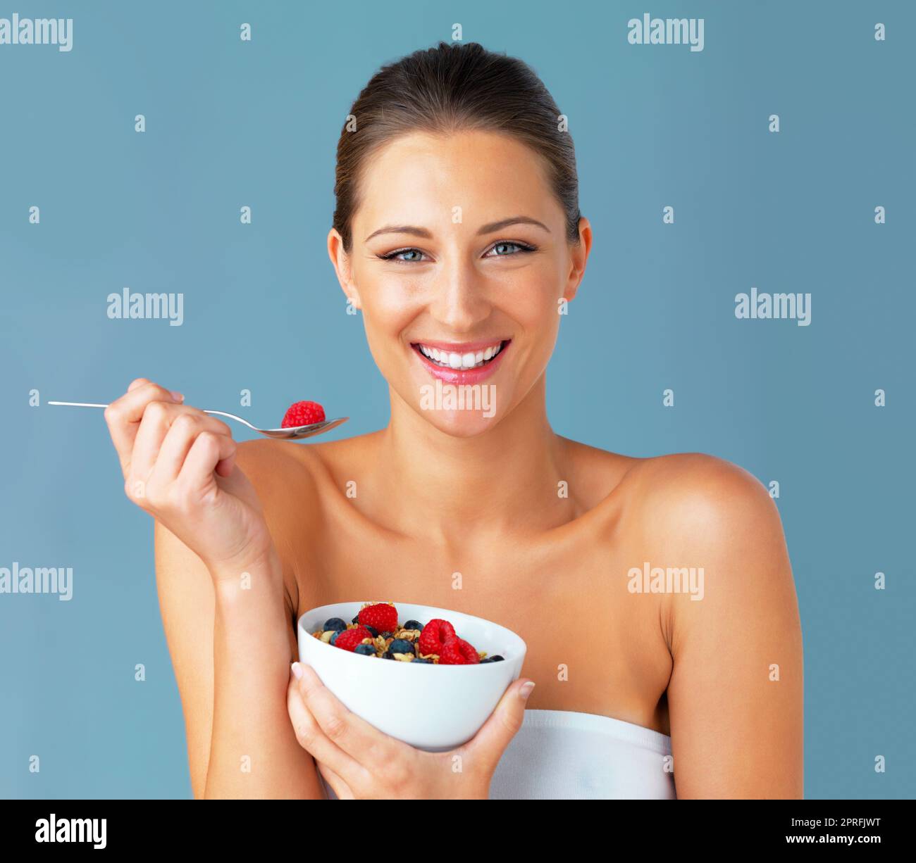 "Quand je mange bien, je me sens bien." Studio photo d'une jeune femme attrayante mangeant un bol de muesli et de fruits sur fond bleu. Banque D'Images