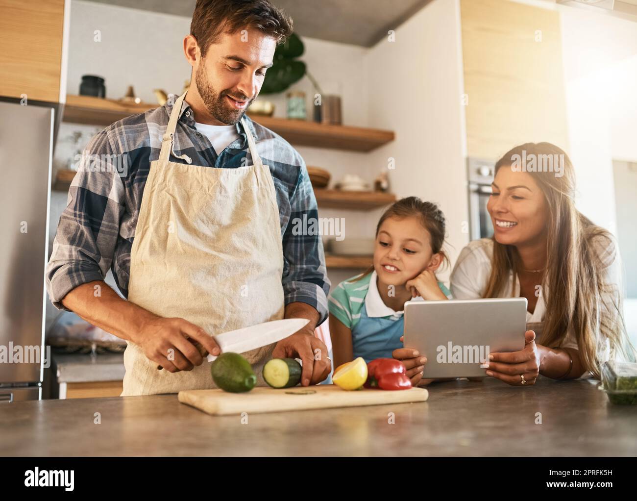 Laissez papa vous montrer comment il a fait. Deux parents heureux et leur jeune fille essayant une nouvelle recette dans la cuisine ensemble. Banque D'Images