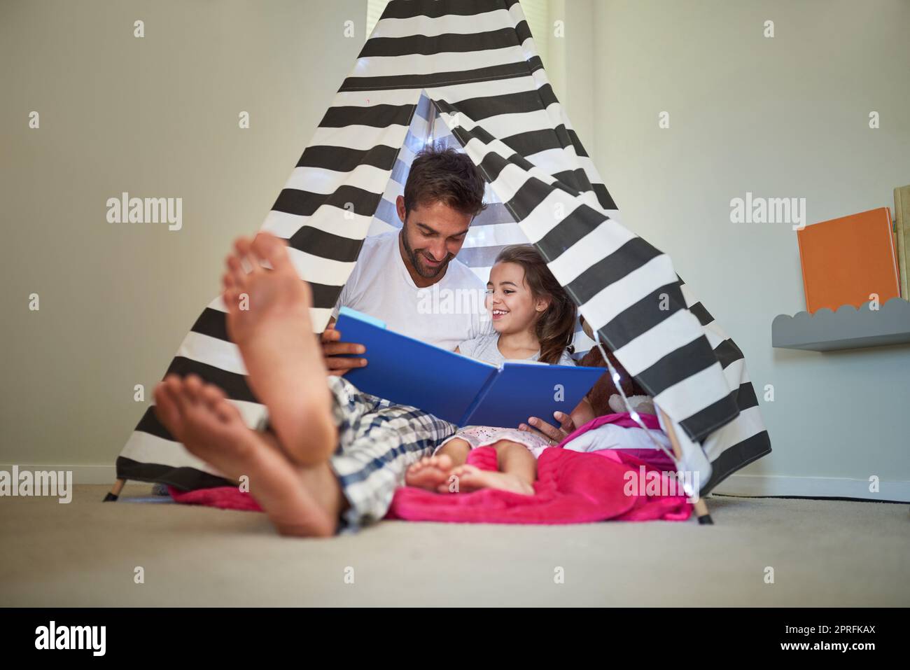 Ils adorent être douillets avec une bonne lecture. Un père lisant un livre avec sa petite fille dans une tente à la maison. Banque D'Images