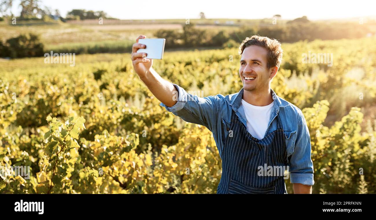 Je veux partager mes progrès. Un jeune homme prenant un selfie avec son téléphone portable tout en travaillant sur une ferme. Banque D'Images
