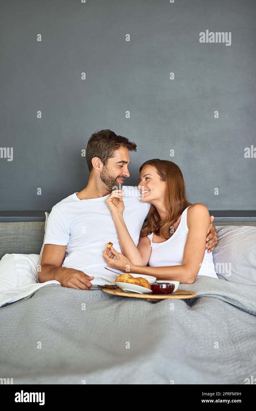 Réveillez-vous, puis dégustez du vin et dînez. Un jeune couple heureux prenant le petit déjeuner au lit à la maison. Banque D'Images