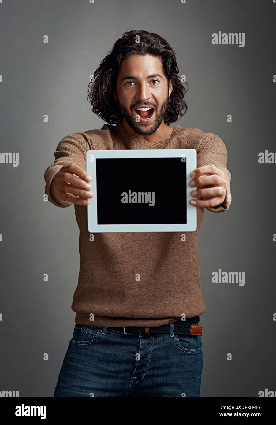 Prenez-le de moi. C'est génial. Photo en studio d'un jeune homme enthousiaste tenant une tablette numérique avec un écran vierge sur fond gris. Banque D'Images