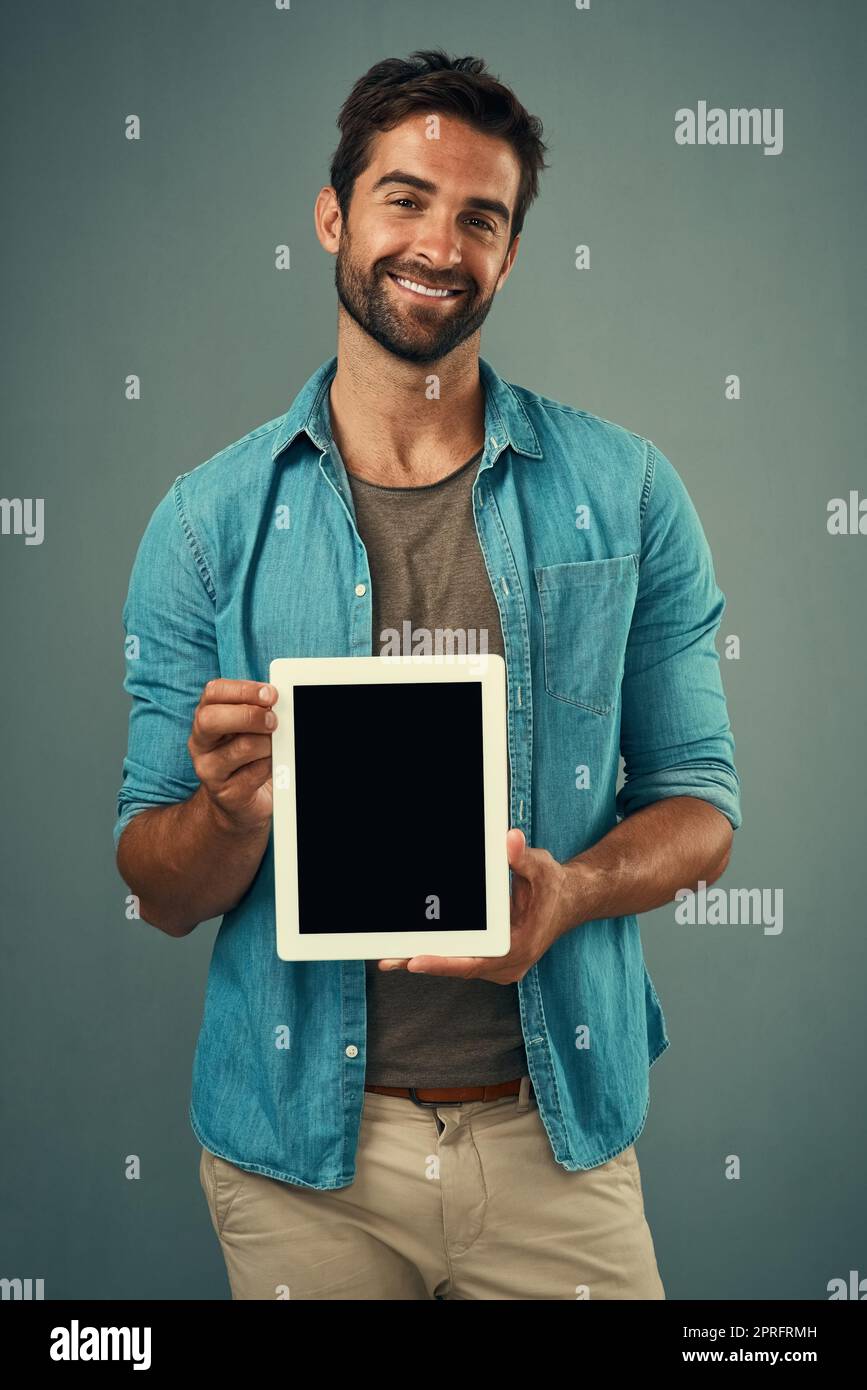 Faisons un peu de buzz en ligne. Portrait studio d'un jeune homme charmant tenant une tablette numérique avec un écran vierge sur fond gris. Banque D'Images
