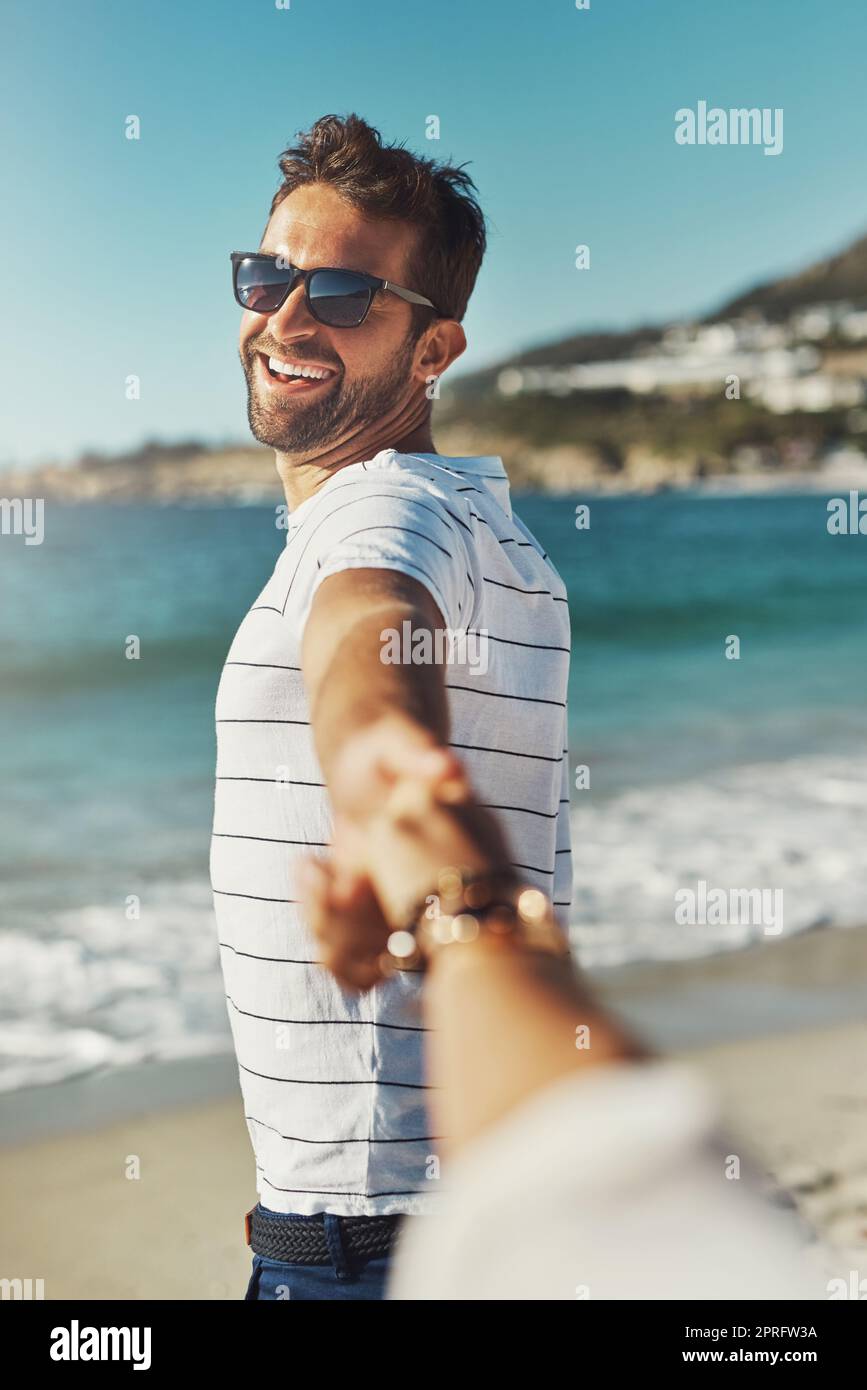 Suivez-moi, au soleil, au sable et à la mer. Un jeune homme tenant ses amies main et menant le chemin à la plage. Banque D'Images