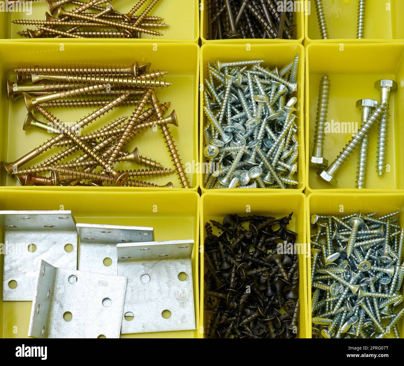 Diverses vis métalliques dans des récipients en plastique jaune séparés. Banque D'Images