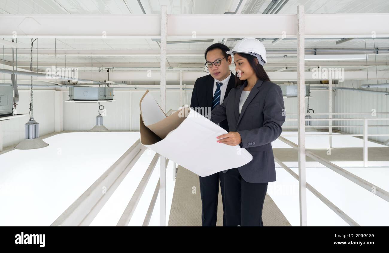 Ingénieur en casque de sécurité tenir le plan de construction du système de ventilation tout en faisant vérifier la propreté de l'usine par l'inspecteur du bâtiment. panneaux d'éclairage et de climatisation montés au plafond. Banque D'Images