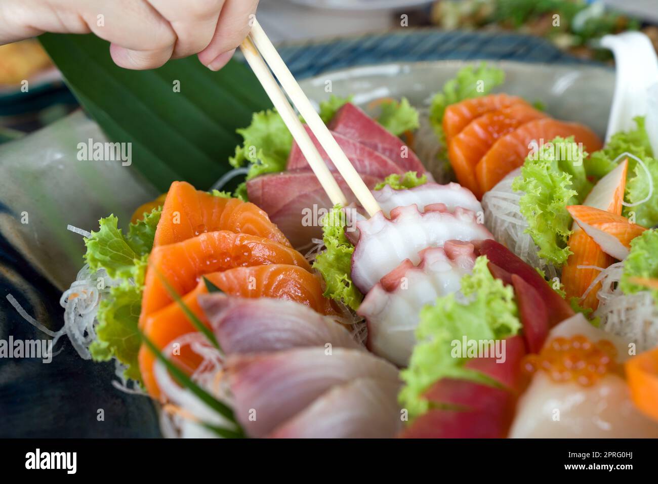 Gros plan tako picking avec baguettes de mélange sashimi dans plaque en céramique. Buffet de cuisine japonaise. Choix du chef : saumon, hamachi, Tako, Hotate et hokkigai Banque D'Images