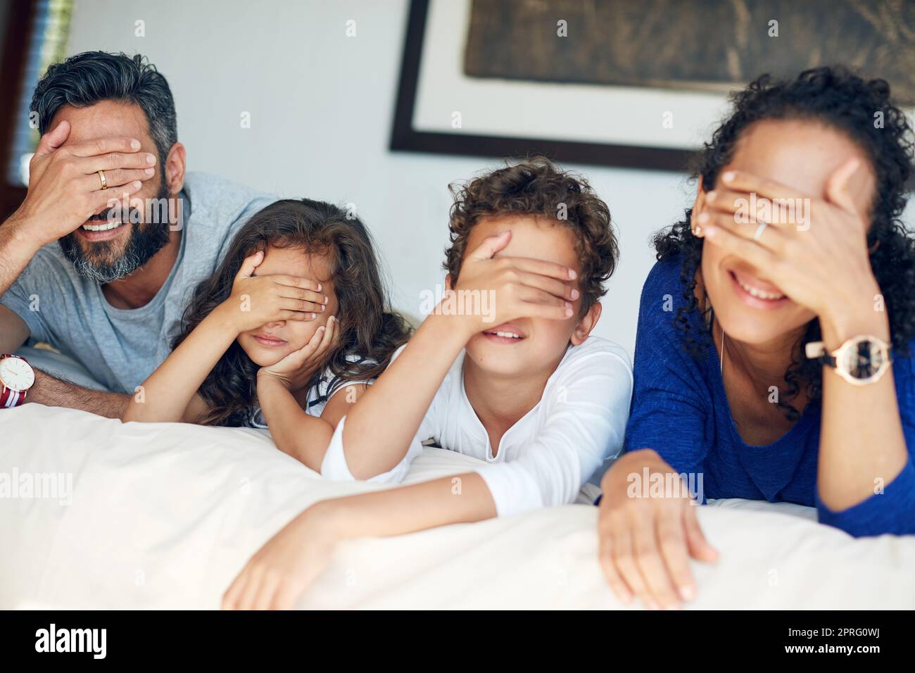 Quelle surprise nous réserve le week-end : une famille qui couvre les yeux tout en étant allongé sur un lit à la maison. Banque D'Images