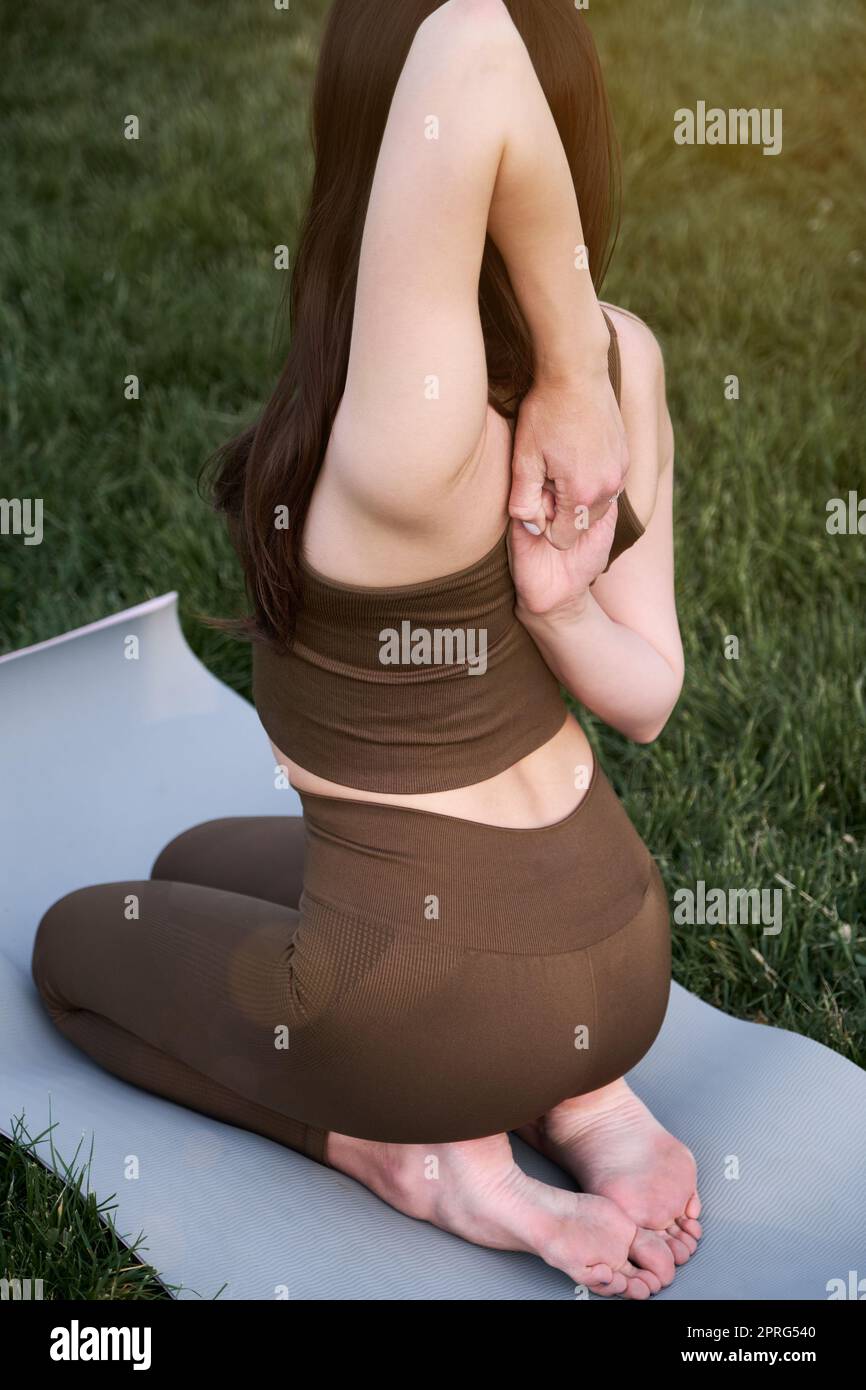 Jeune belle femme pratiquant le yoga à l'extérieur dans le parc assis sur un tapis. Banque D'Images