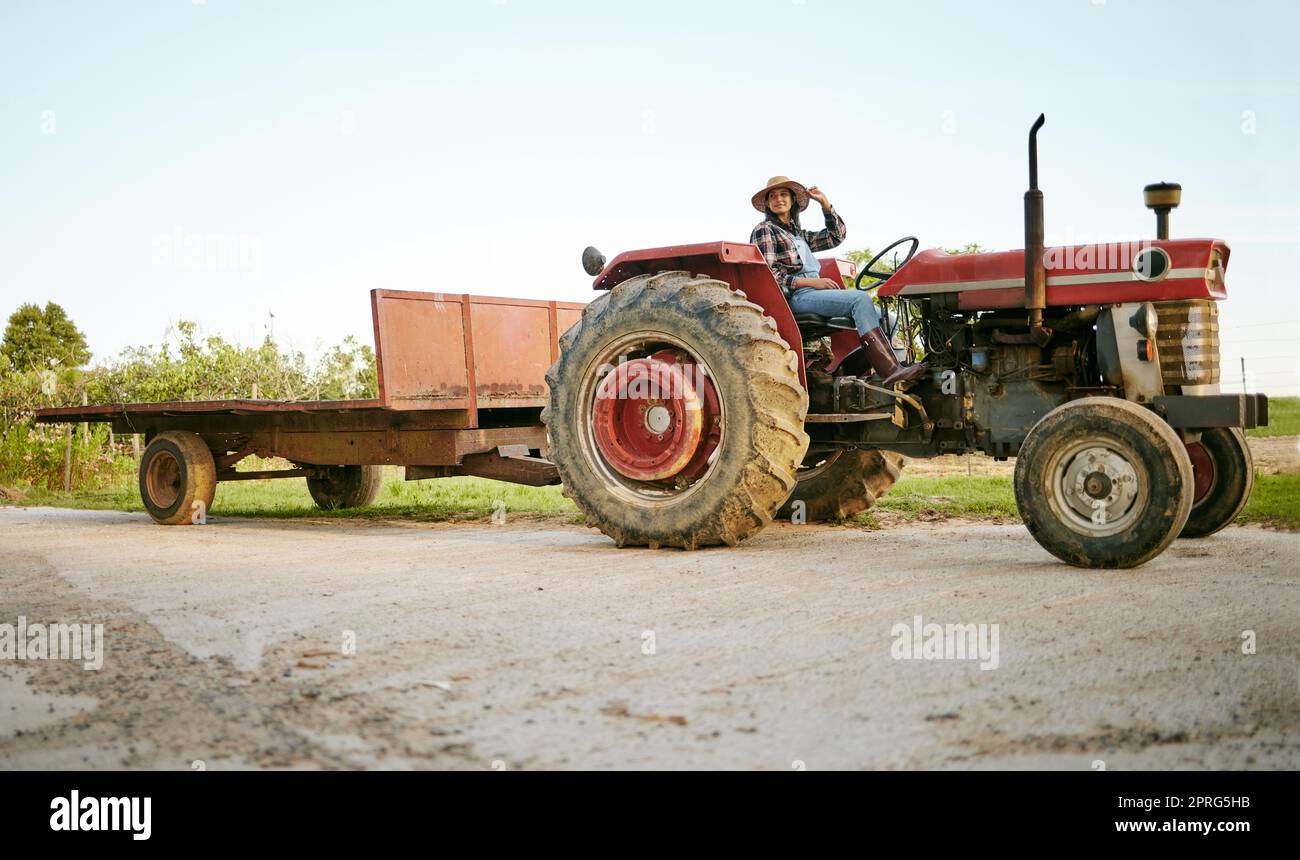 Exploitation agricole, tracteur et agriculture avec une femme heureuse agriculteur conduisant un véhicule à la ferme pour la durabilité, la croissance et le développement dans un environnement durable et vert. Récoltes agricoles pendant la saison de récolte Banque D'Images