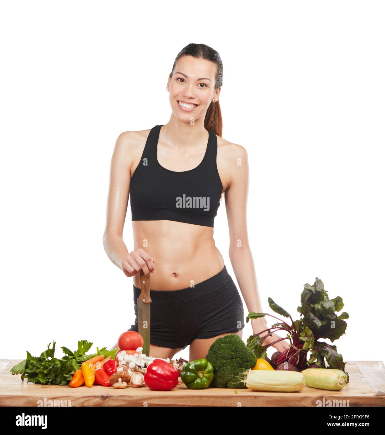 Se sentir bien au sujet des choix sains. Studio portrait d'une jeune femme attrayante posant avec une table pleine de légumes sur un fond blanc. Banque D'Images