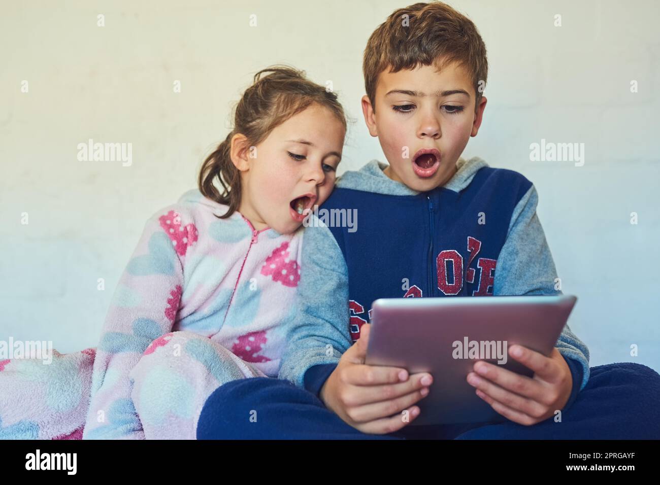 Incroyable. Deux jeunes frères et sœurs ont l'air surpris lorsqu'ils utilisent une tablette numérique à la maison. Banque D'Images