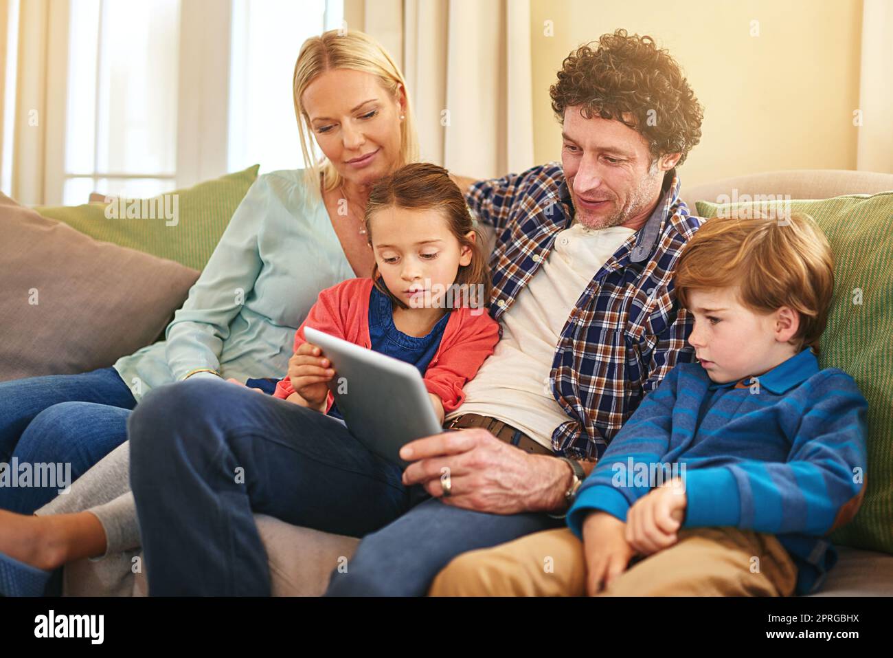 C'est une famille technophiles qui navigue ensemble sur une tablette numérique à la maison. Banque D'Images