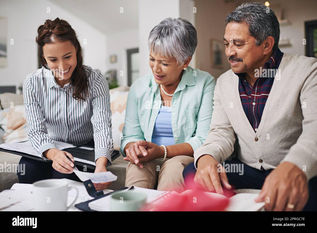 Vous pourriez économiser ce montant chaque mois. Un jeune représentant d'assurance présentant un produit à des clients âgés dans leur maison. Banque D'Images