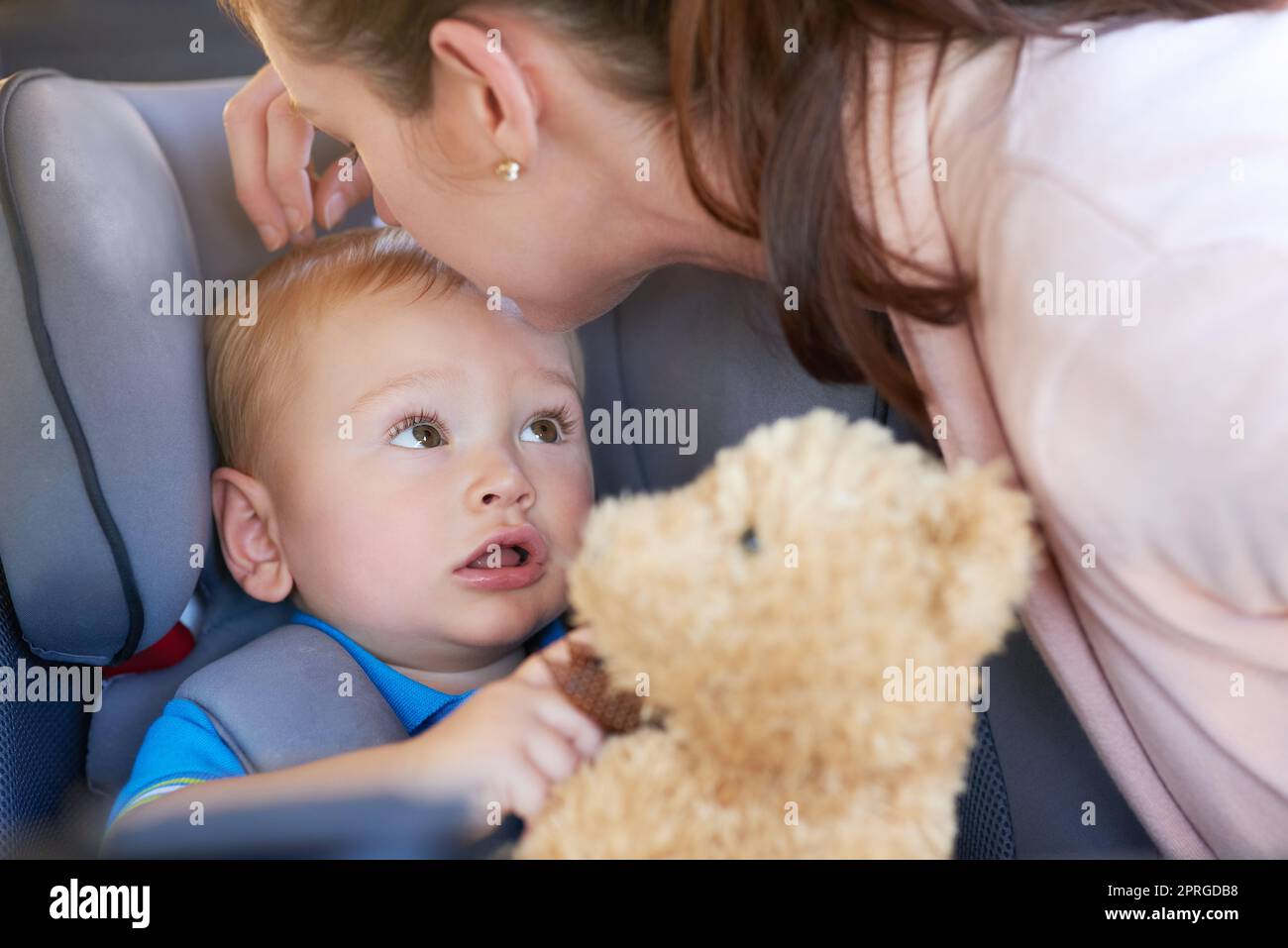 J'espère qu'il s'est arrêté à la boutique de jouets, maman. Une mère embrassant son bébé garçon assis dans un siège de voiture. Banque D'Images