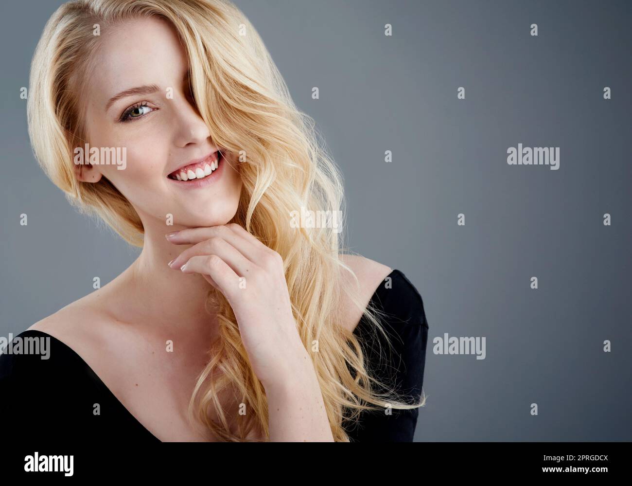 Des cheveux magnifiques et un grand sourire. Studio portrait d'une jeune femme attrayante avec de beaux cheveux blond longs posant sur un fond gris. Banque D'Images