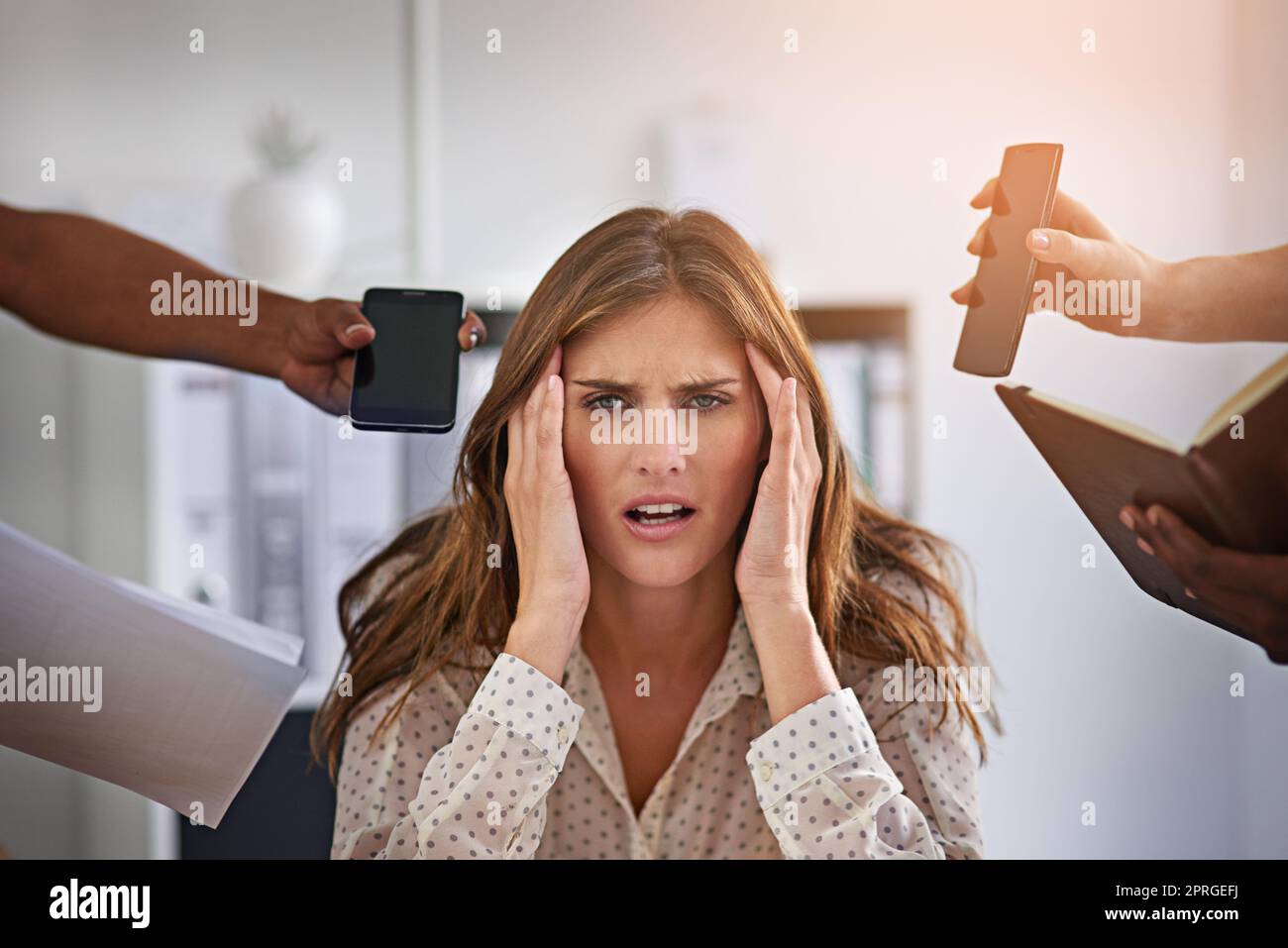 Trop stressée pour se concentrer : une femme d'affaires à l'aspect anxieux entourée de mains qui se mettent en main pour tenir des articles de bureau. Banque D'Images