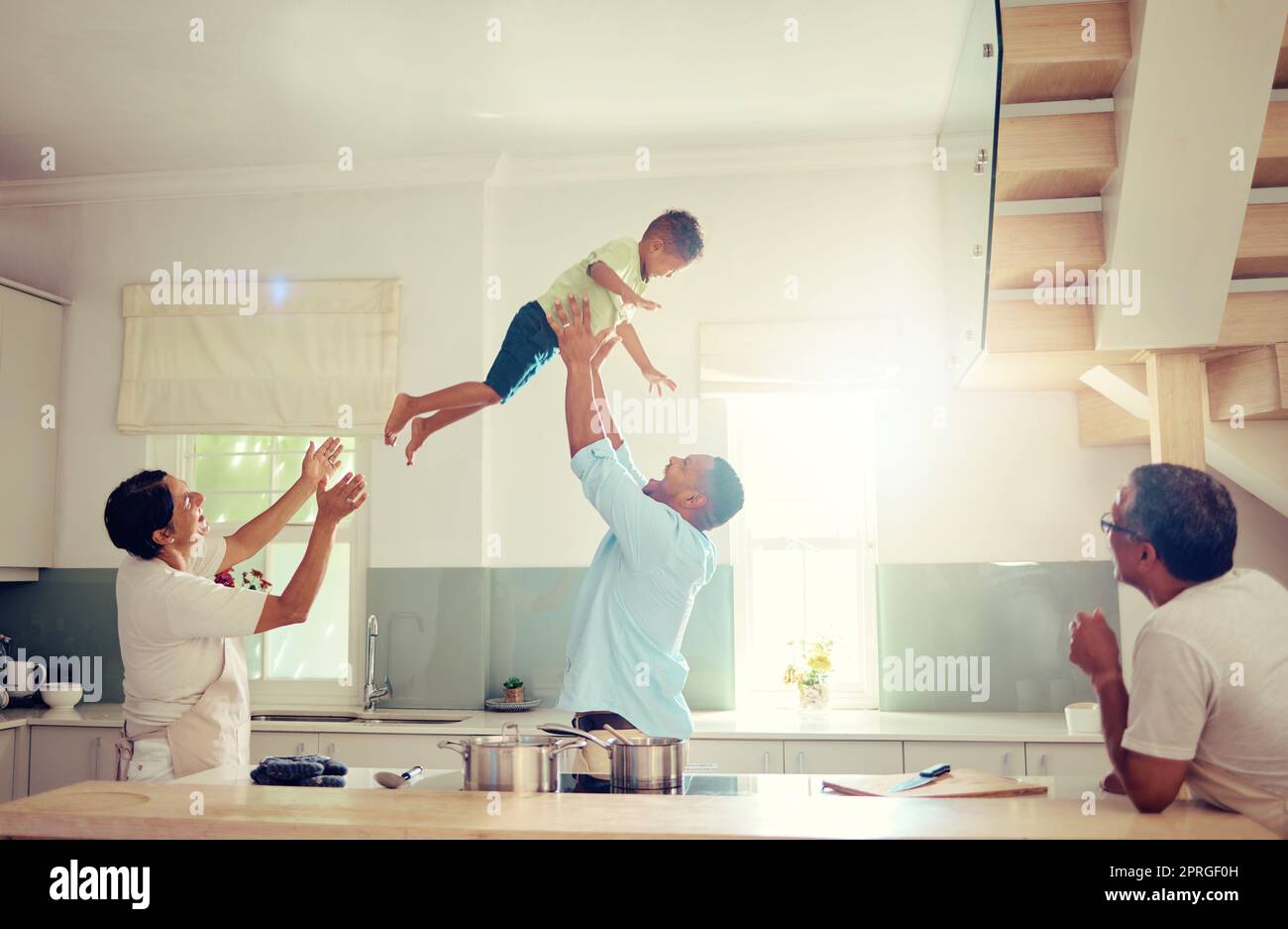 Famille heureuse, maison et père amour d'un homme avec son enfant dans l'air jouant dans une cuisine maison. Génération d'hommes sourient à la maison avec un moment amusant ensemble et se détendre et esprit comique avec le soleil brillant Banque D'Images