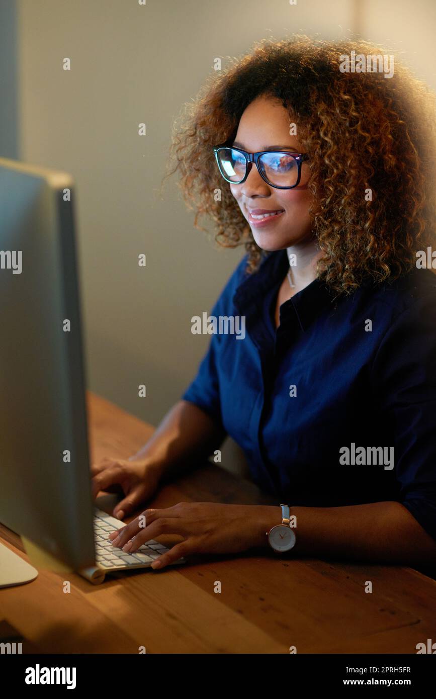 Combait de rattraper ses délais. Une jeune femme d'affaires travaillant tard sur un ordinateur dans un bureau. Banque D'Images