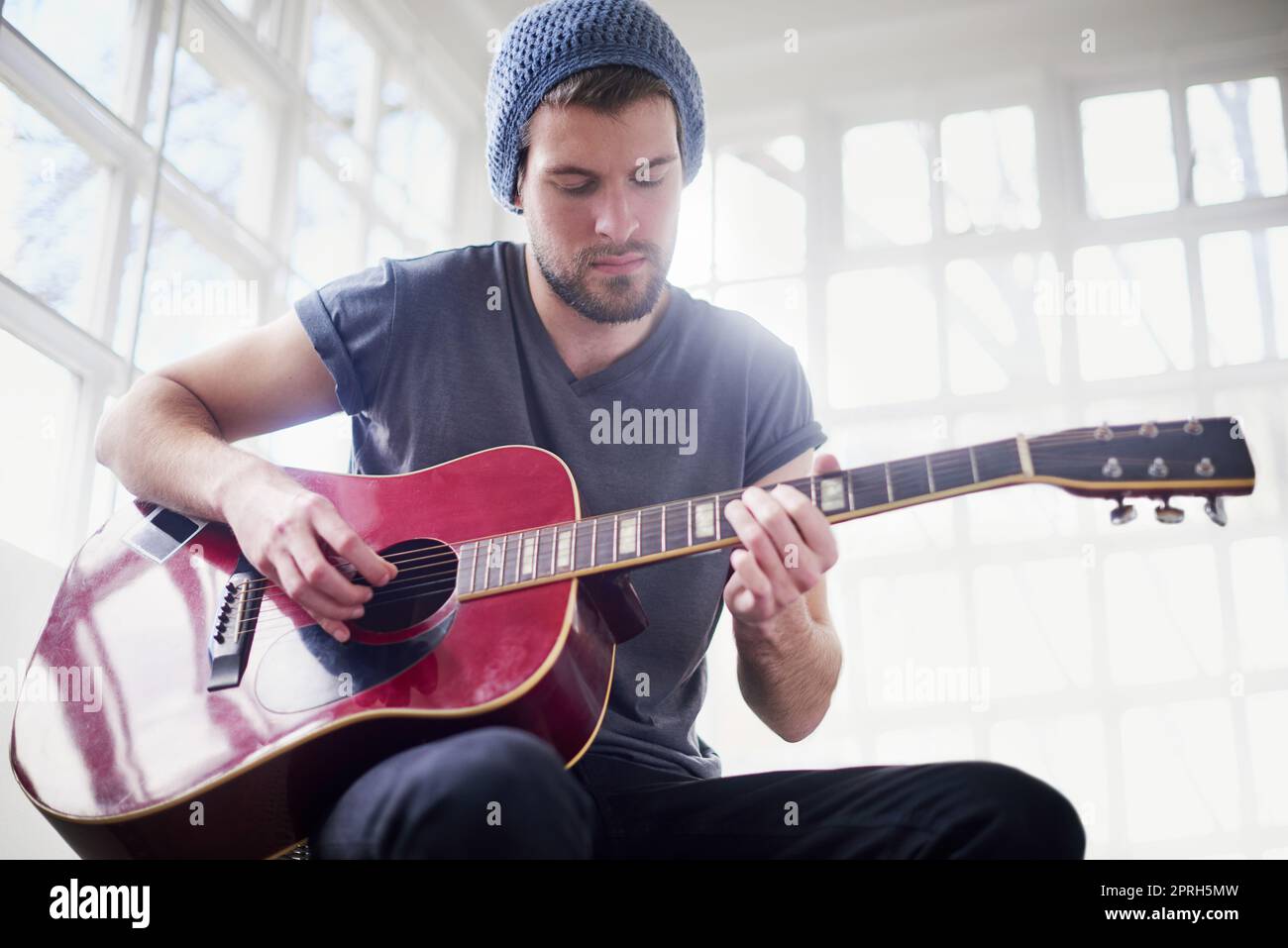 Maîtriser un nouvel accord. Un beau jeune homme jouant de la guitare à la maison. Banque D'Images