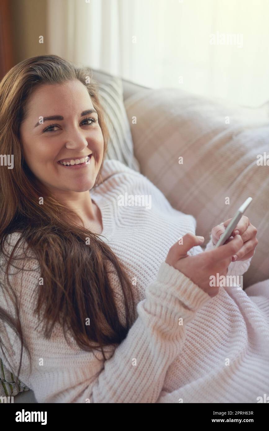 Prêt pour le week-end et un moment de détente. Portrait d'une belle jeune femme qui envoie des SMS sur son téléphone portable à la maison. Banque D'Images